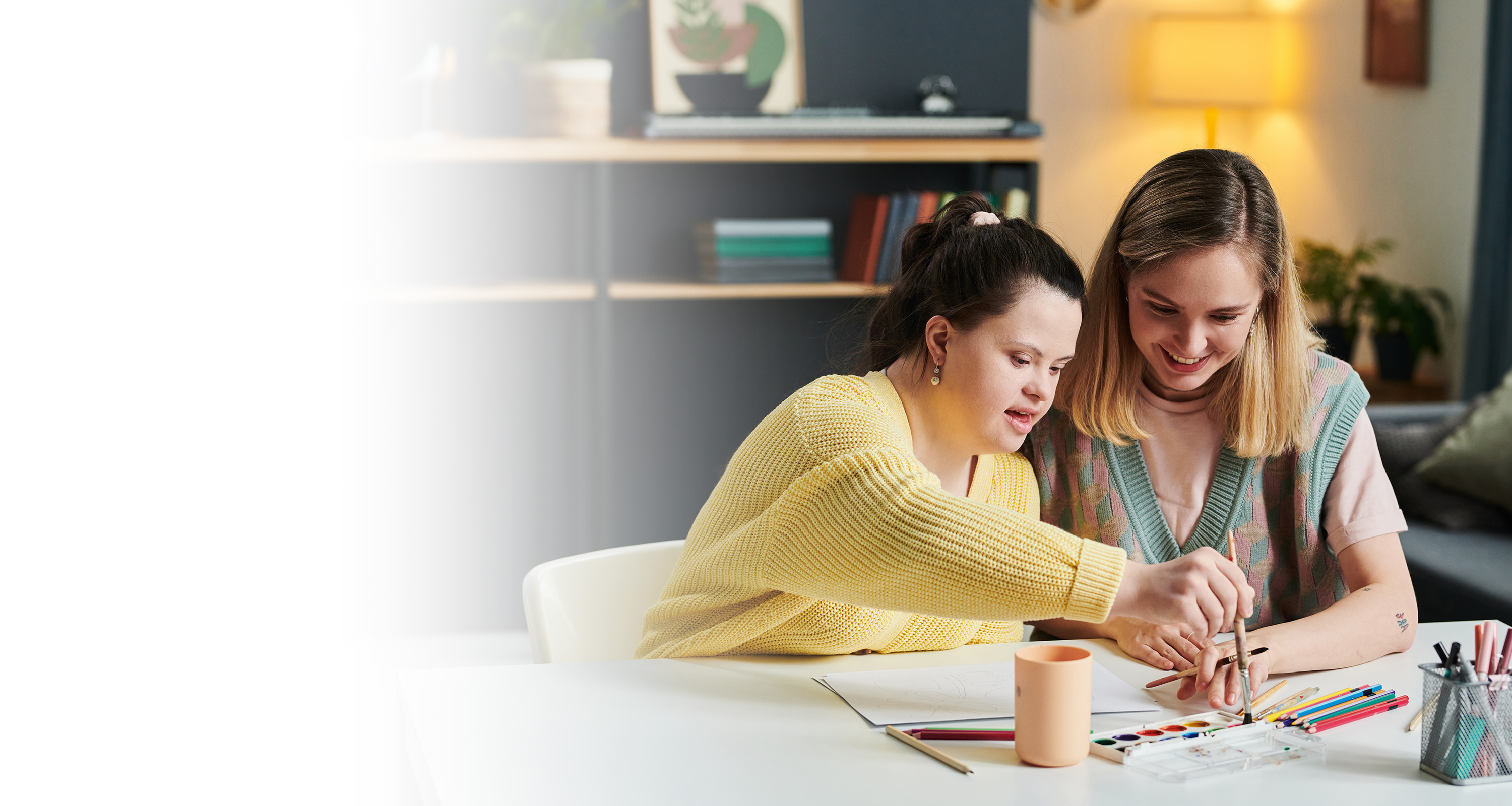 2 girls, one with Down syndrome, colouring and smiling.